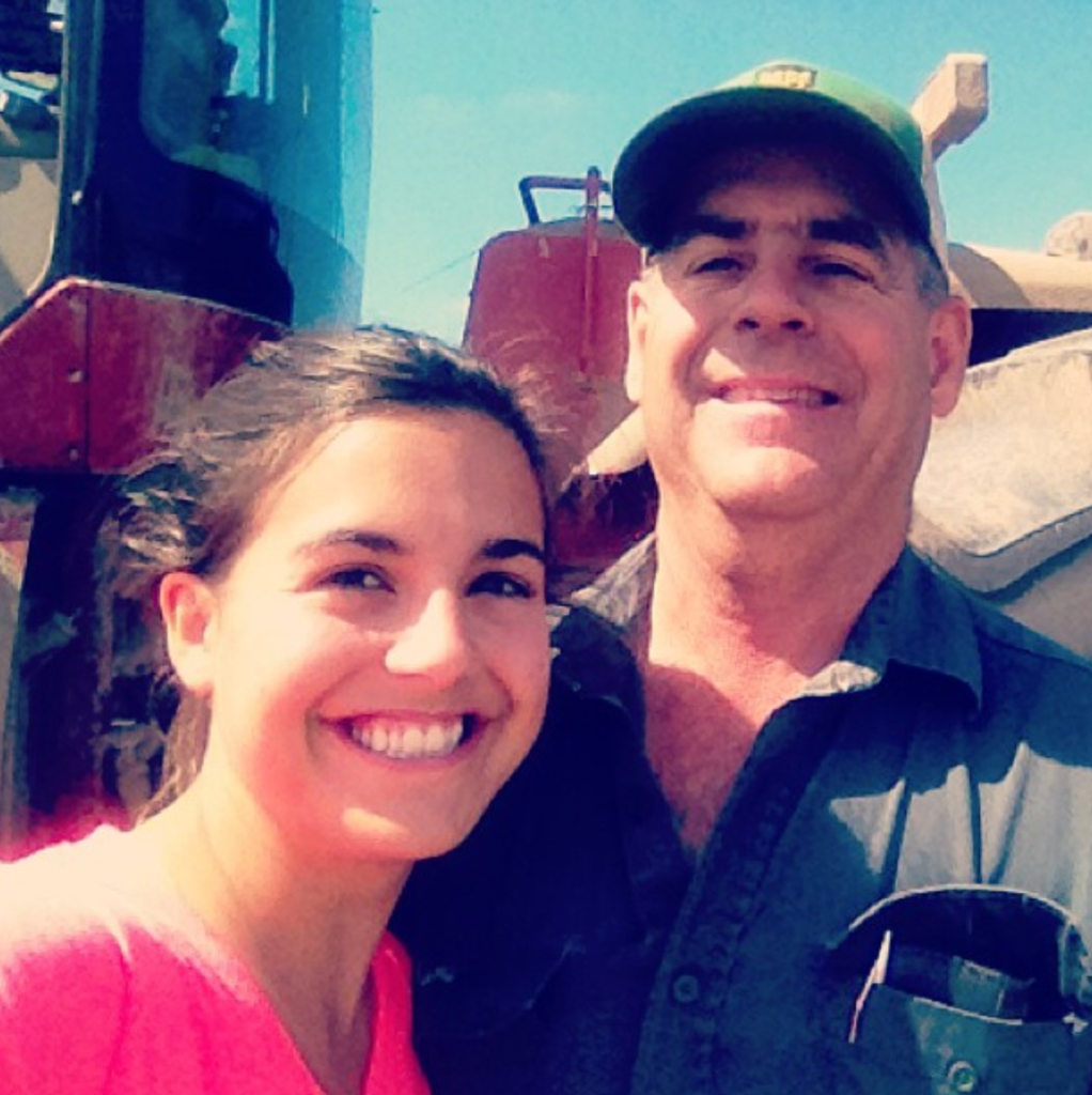 Jordyn and her dad standing in front of a tractor, smiling together. 