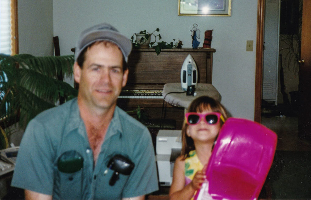 Jordyn, the author, as a child, sits next to her dad in his work uniform.
